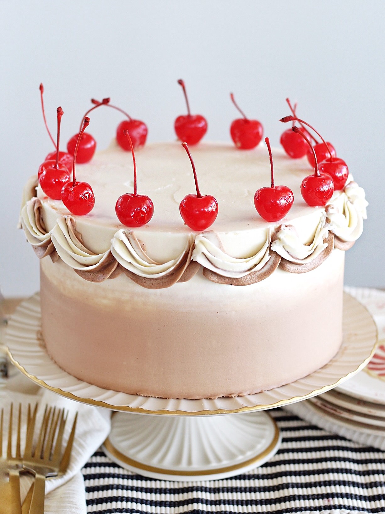 A coca cola cake on a cake stand with cherries on top.