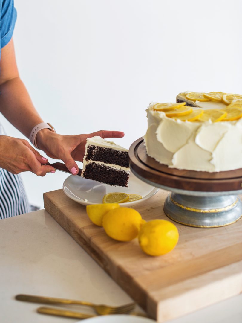 Cake by Courtney - Chocolate Lemon Zucchini Cake #chocolatecake #chocolatezucchinicake #lemoncreamcheesefrosting #chocolatelemonzucchinicake Woman placing cake slice on a plate.