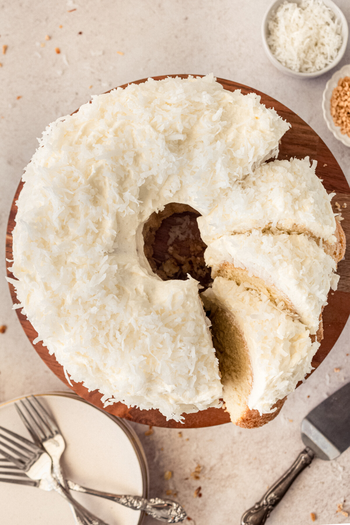 A coconut bundt cake with slices cut into it on a cake stand with plates and forks on the table.