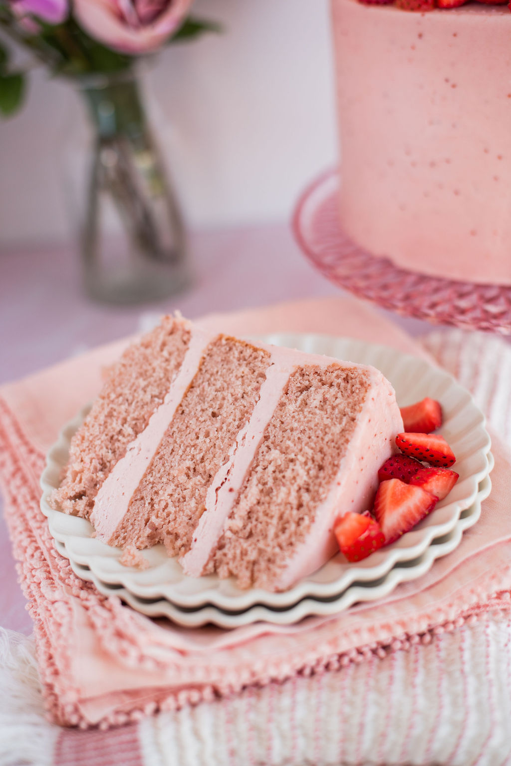 A slice of strawberry cake on a plate with pink towels under it.