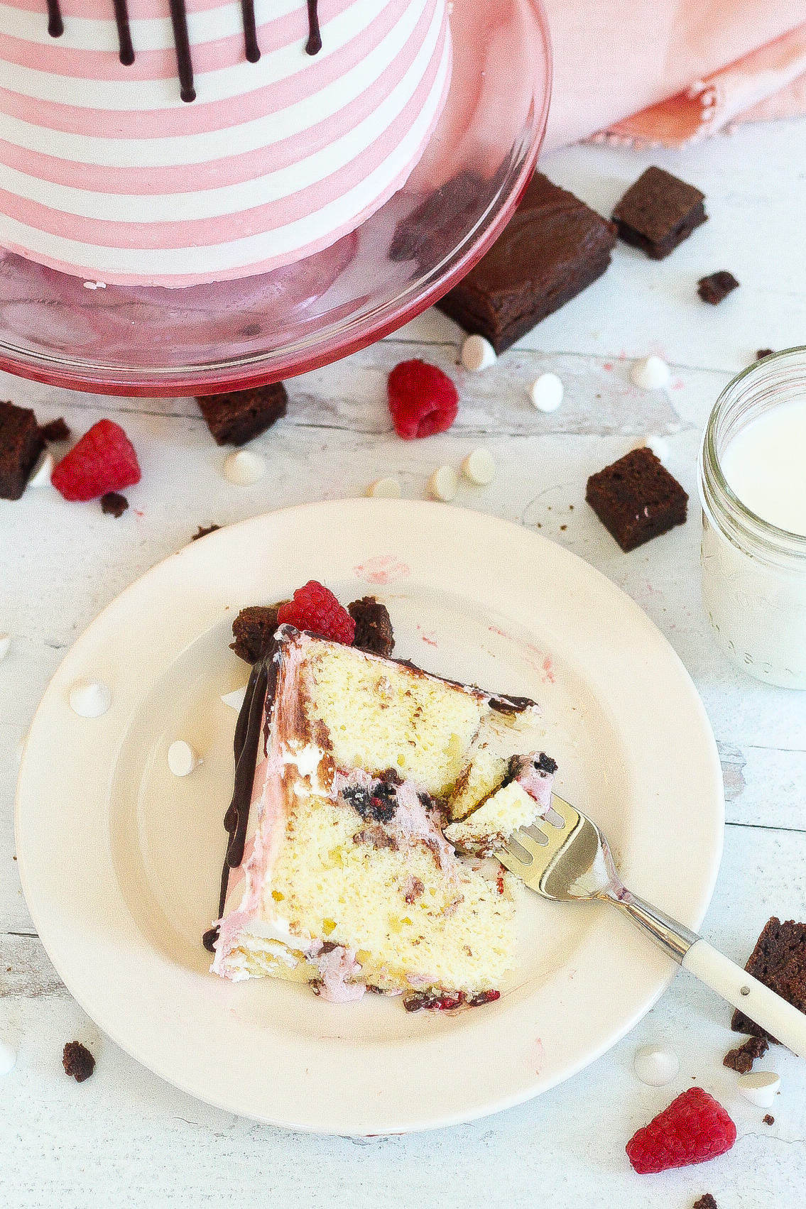 White chocolate raspberry brownie cake on a plate with a bite taken out.