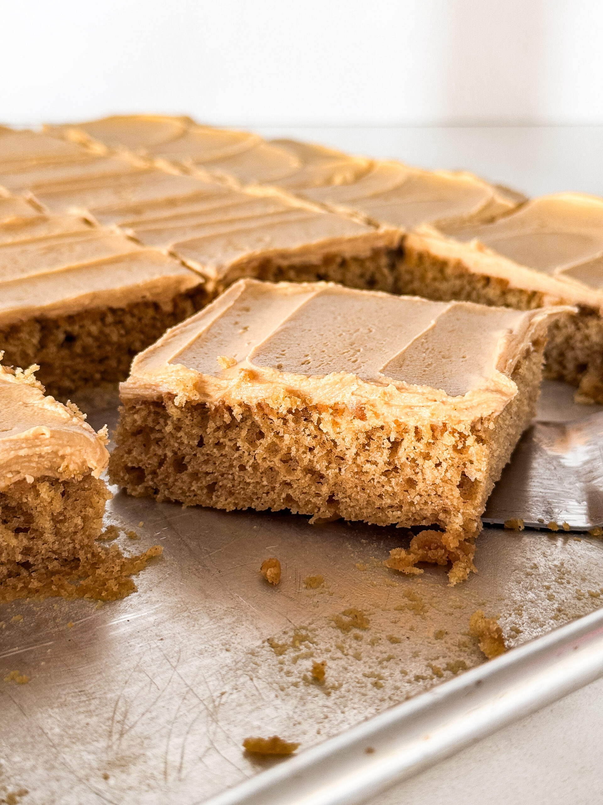 Slices of peanut butter sheet cake on a jelly roll pan with a spatula under one slice of cake.