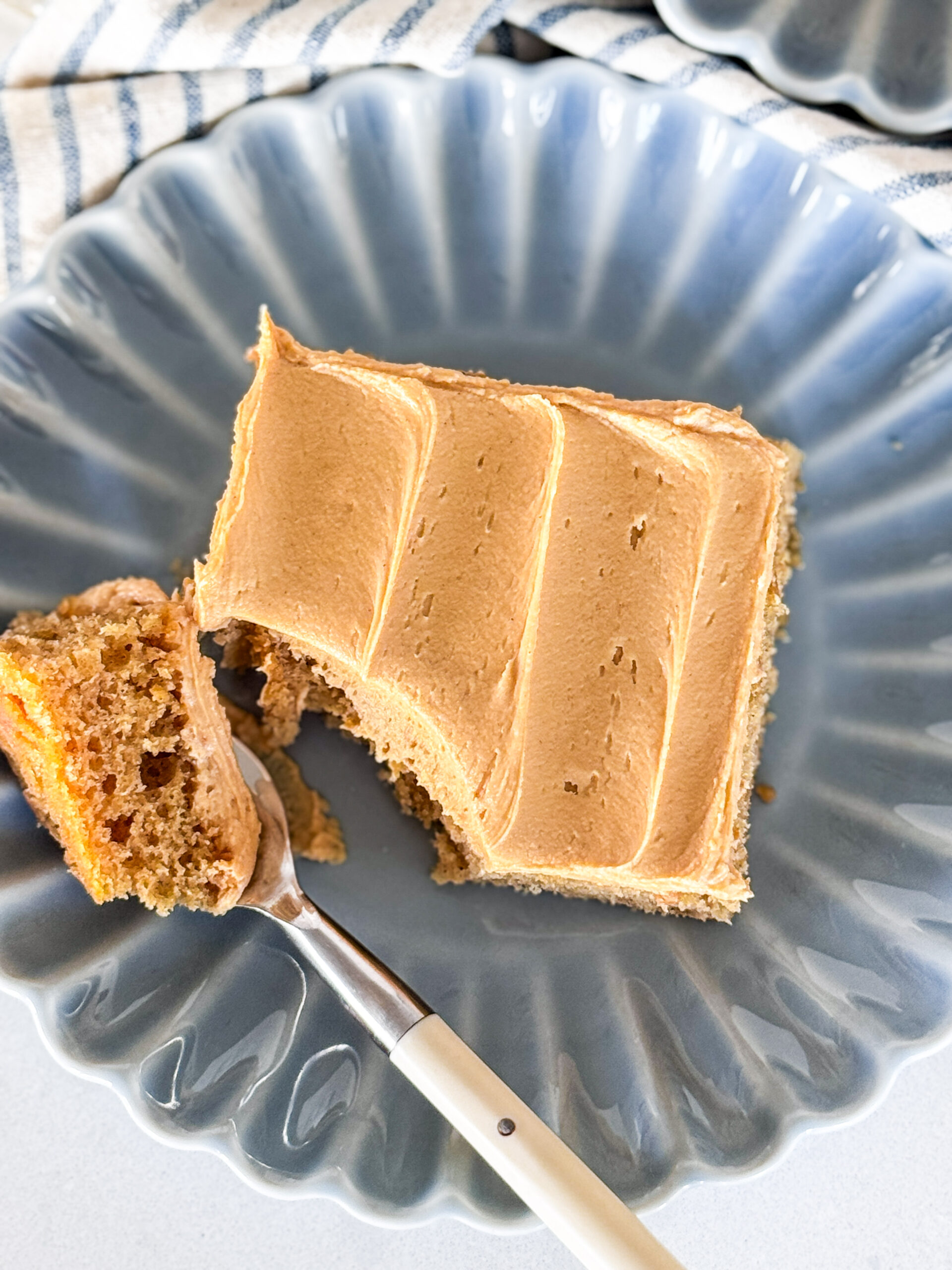 A slice of Peanut Butter Sheet Cake on a blue scalloped plate with a bite of the cake on a fork.