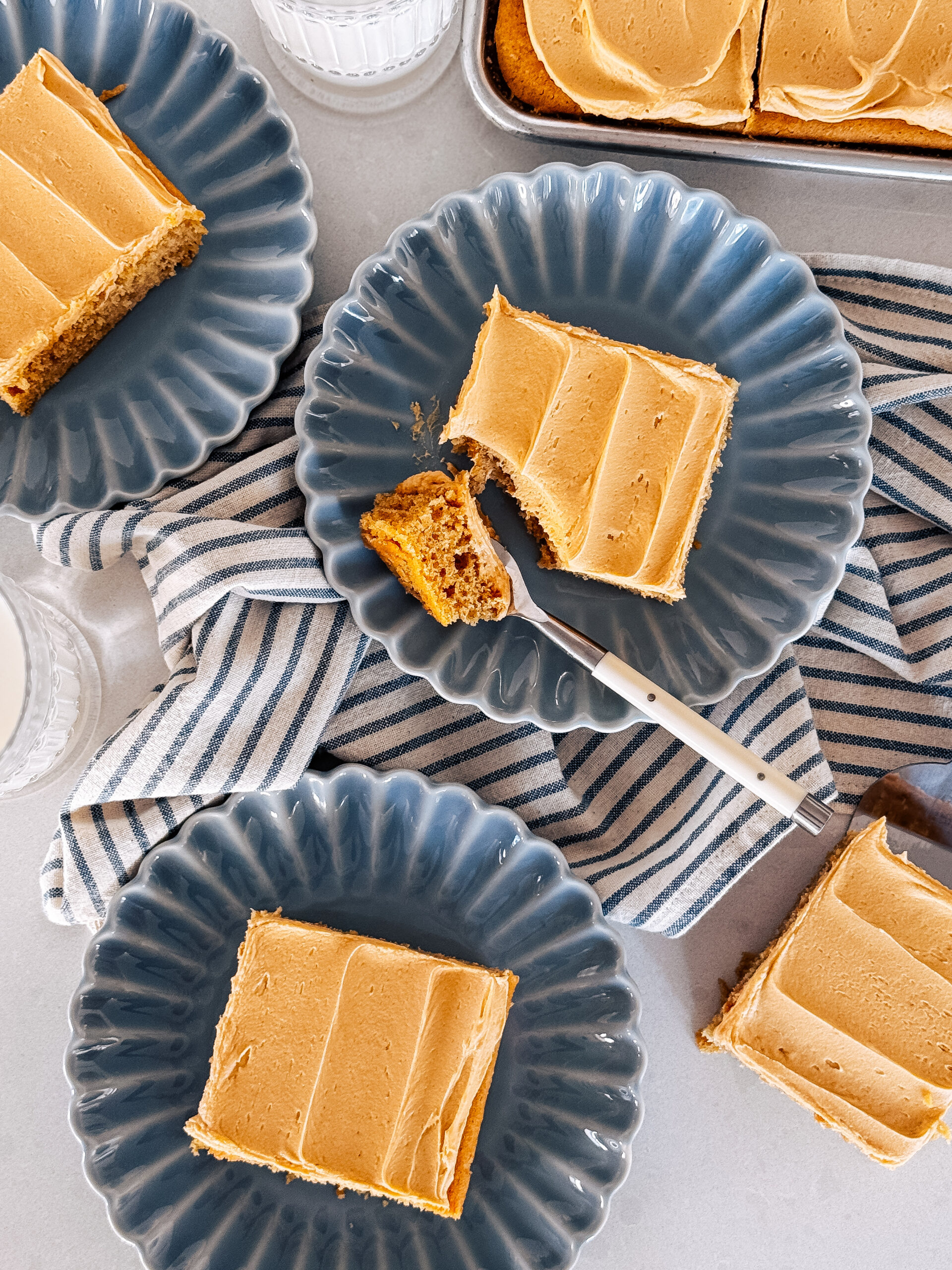 Four slices of peanut butter sheet cake on blue plates with a towel underneath them.