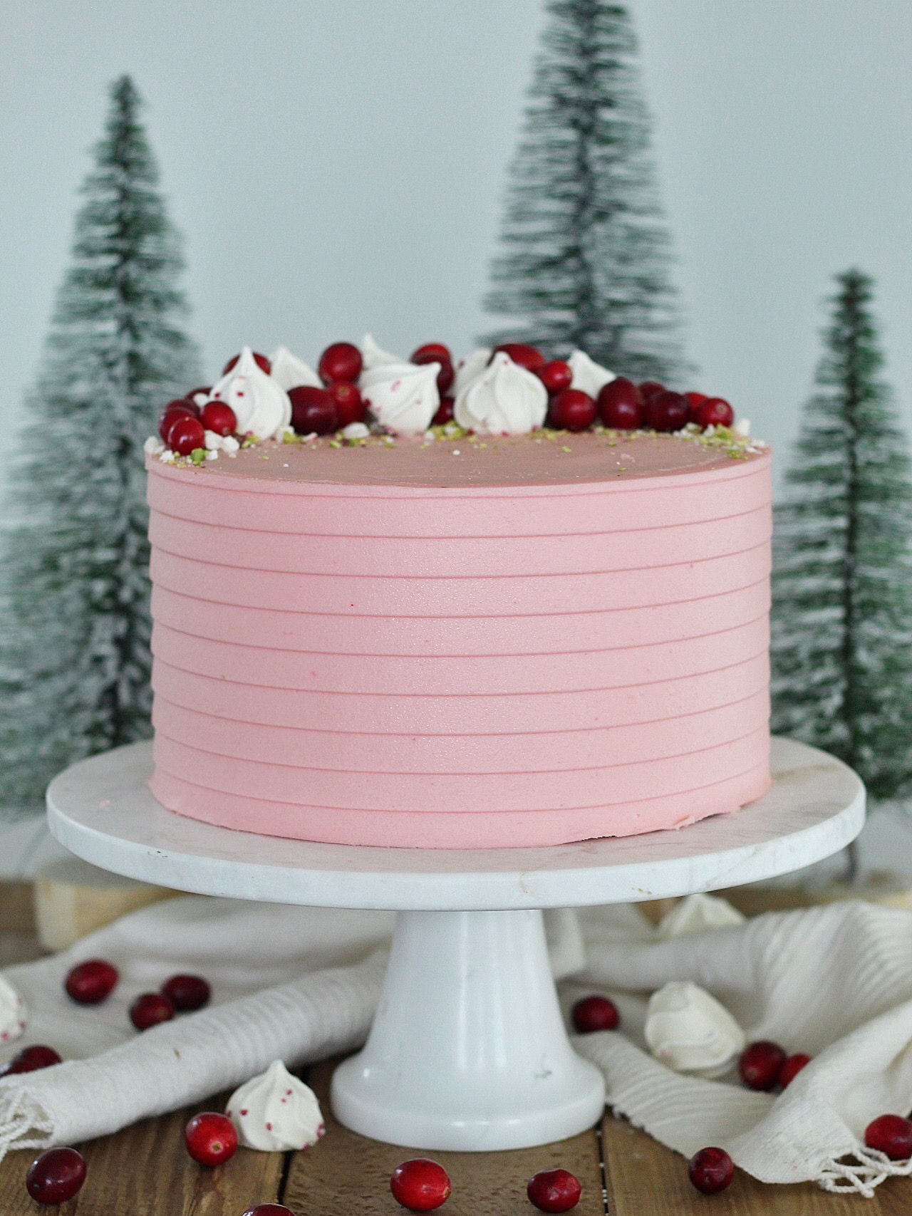 Pink cake on a cake stand with trees around it.