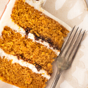 A three layer cake slice on a plate with a fork.